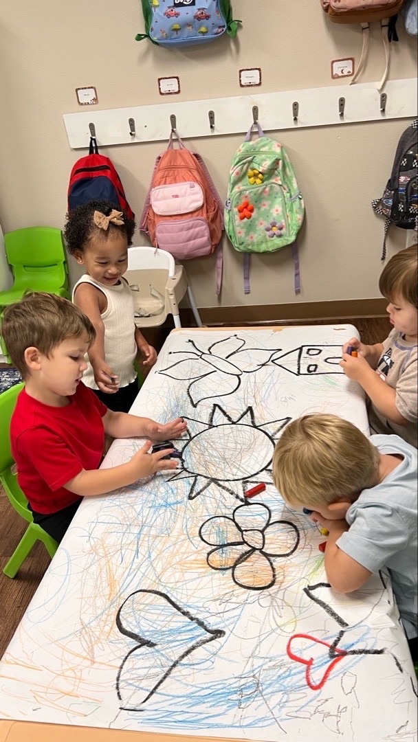 Two young children playing together with colourful stacking toys at a classroom table.